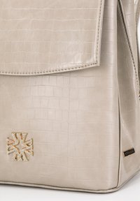Bolso de imitación de cuero beige con estampado de cocodrilo, tapa plegable, detalles de hardware dorado y un logotipo metálico de marca en la parte frontal.