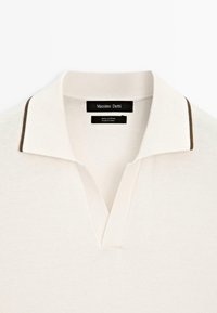 Polo shirt in cotone color crema con scollo a V e profilo marrone a contrasto lungo il colletto. L'etichetta riporta "Massimo Dutti."