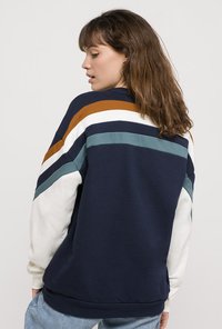 Mørkeblå sweatshirts med iøjnefaldende horisontale striber i hvid, orange og teal. Har en afslappet pasform samt ribbede manchetter og kant.