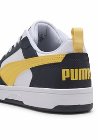 PUMA sneakers med et farveskema i hvid, navy og gul, læderoverdel, gummisål og logodetalje på hælen.