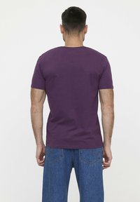 Korte mouwen paarse t-shirt van zachte stof, met een ronde halslijn en een klassieke pasvorm. Draagt met blauwe spijkerbroek.