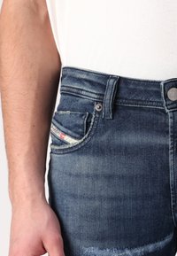 Mörkblå denimjeans för män med en slitna struktur. Funktioner inkluderar en liten framficka, metallknapp och synliga söm detaljer.