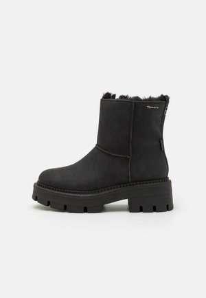 Bottines noires à la cheville avec une tige synthétique texturée, doublure en peluche au niveau du col et une semelle en caoutchouc épaisse avec un motif de bande de roulement.