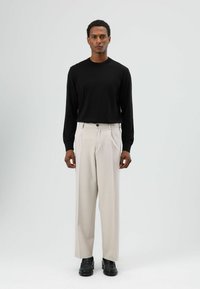 Zwart shirt met lange mouwen, beige geplooide broek en zwarte schoenen. Eenvoudig ontwerp met een ontspannen pasvorm en licht stof.