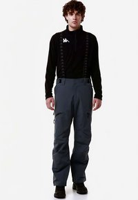 Pantaloni da sci grigi con bretelle regolabili, due tasche con cerniera e vestibilità ampia, abbinati a una maglia nera a maniche lunghe con un logo.