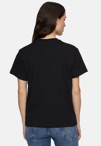 Zwarte katoenen t-shirt met korte mouwen en een ronde hals, met een eenvoudige achterkant en een relaxte pasvorm, gecombineerd met blauwe denim jeans.