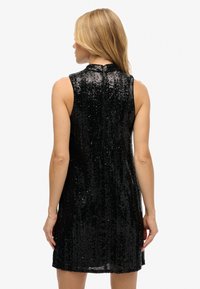 Czarna sukienka bez rękawów pokryta cekinami, z wysokim dekoltem i prostym krojem. Widoczny zamek błyskawiczny z tyłu. Gładka faktura.