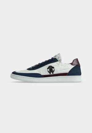 Sneaker bianco low-top con dettagli blu navy e marrone, logo nero sul lato e suola bianca, visto dal lato esterno.