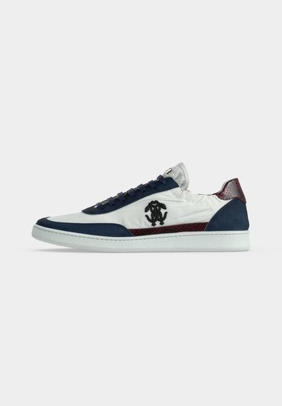 Baskets basses blanches avec des accents bleu marine et marron, logo noir sur le côté et semelle blanche, vues de l'extérieur.