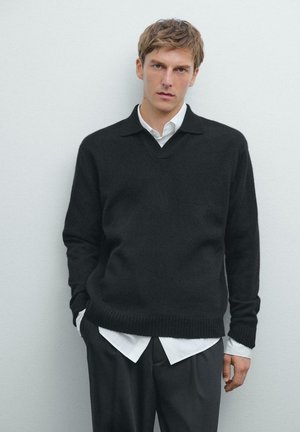 Black v-neck sweater made of soft knit material, with ribbed cuffs and hem, layered over a white collared shirt, paired with dark trousers.