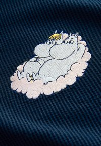 Parche bordado que presenta a dos personajes de dibujos animados acurrucados en una nube rosa, sobre un tejido azul oscuro texturizado.