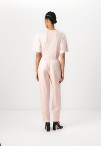 Light pink jumpsuit with short sleeves, elastic waistband, and tapered legs; paired with black high-heeled shoes. Smooth fabric texture.