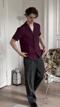 Korte mouwen, bordeaux kleurige button-up shirt gecombineerd met loszittende, leisteenkleurige broek. Het shirt heeft een ontspannen kraag en een subtiele textuur.