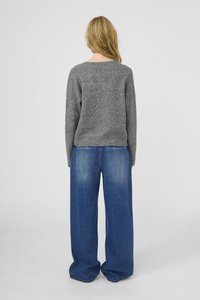 Sivý vlnený sveter s okrúhlym výstrihom v kombinácii s voľnými modrými džínsami s širokými nohavicami a vyblednutým umývaním, z pohľadu zozadu.