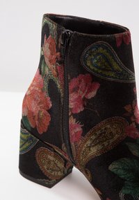 Zwarte enkelboots met een bloemen- en paisleypatroon, stoffen textuur en een zijrits. Chunky hak met een gladde zwarte zool.