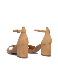 Tan suede heeled sandals with a rounded open toe, adjustable ankle strap, and a chunky block heel. Smooth texture and minimal design details.