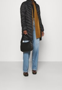 Svart puffjacka, brun ribbad tröja, ljusblå vida jeans och en vävd svart handväska bärs med mörkbruna skor.