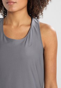 Canotta sportiva grigia con una texture a coste, caratterizzata da un logo discreto sull'area del petto e spalline larghe per comfort e mobilità.