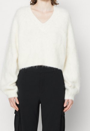 Femme portant un pull blanc duveteux à col en V avec manches longues et un pantalon cargo noir taille haute.