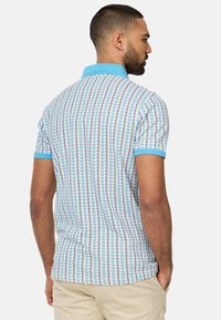 Kortærmet polo-shirt i lys blå med et geometrisk mønster. Har en ensfarvet blå krave og kant, lavet af åndbart stof.