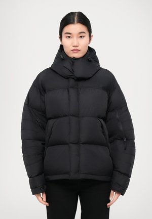 Black padded jacket features a high collar, zippered pockets, and a boxy shape with quilted surface for insulation and warmth.