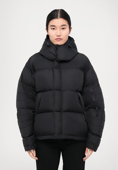 Die schwarze gepolsterte Jacke verfügt über einen hohen Kragen, Reißverschluss-Taschen und eine kastige Form mit einer gesteppten Oberfläche für Isolierung und Wärme.