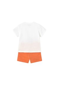 Camiseta blanca de manga corta con dobladillo deslavado combinada con pantalones cortos naranjas. Tela de algodón, diseño simple y corte casual.