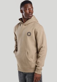 Beige hooded sweatshirt in soft fabric, featuring a front pocket and a spiral logo on the left chest area. Long sleeves with ribbed cuffs.