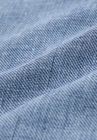 Gros plan d’un tissu bleu doux avec une texture fine et serrée ainsi qu’une couture diagonale subtile créant de douces plis.