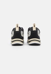 Pari sneaker hitam dan beige yang ditampilkan dari belakang, menampilkan tab tarik beige dengan kata "FLAME" dalam huruf hitam.