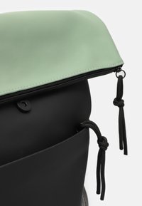 Svart vattentålig ryggsäck med en mintgrön klaff, dragkedjestängning och svart snodd. Har släta material och kontrasterande texturer.