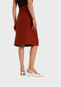 Décolleté bianchi con punta appuntita, tacco piccolo e un accento in metallo dorato. Indossati con un vestito color ruggine a lunghezza ginocchio.