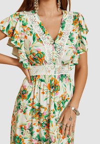 Vestido floral de manga corta con una base blanca y patrones verdes, naranjas y rosas. Detalles de encaje en el escote y la cintura.