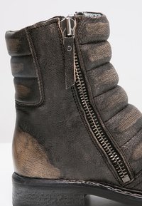 Černé kožené kotníkové boty s prošívanou texturou, bočním zipem se metalickými zuby a texturovanou černou podrážkou. Ošuntělý vzhled.