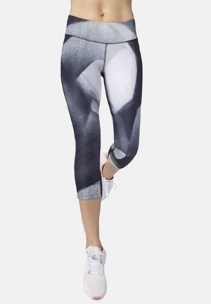 Woman wearing black, white, and gray patterned cropped athletic leggings and white sneakers, standing with one leg slightly raised.