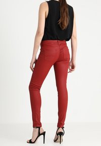 Pantalones ajustados rojos de tela elástica, con cintura alta y bolsillos traseros, combinados con sandalias de tacón negras.