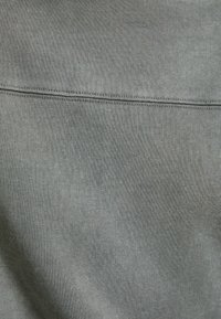 Tissu de sweat-shirt gris avec une surface lisse et légèrement texturée. Présente une couture horizontale dans la partie supérieure.