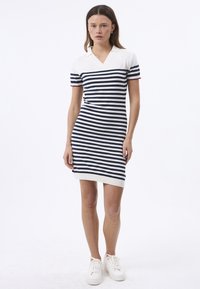 Abito polo a maglia con strisce orizzontali blu navy e bianche, maniche corte, scollo a V e una silhouette aderente con orlo sopra il ginocchio.