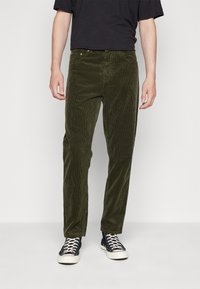 Groene corduroy broek met verticale ribbels, rechte pasvorm, vijf-pocket ontwerp en metalen accenten, gecombineerd met zwarte sneakers.