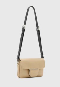 Borsa a tracolla in pelle beige con una forma strutturata, chiusura a pattina e accessori in metallo argentato. Caratterizzata da una tracolla nera regolabile.