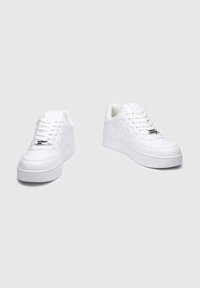 Sneakers bianchi realizzati in materiale sintetico liscio, con un motivo testurizzato, punta rotonda, suola piatta e lacci piatti con etichetta in argento.