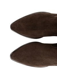 Brązowe zamszowe botki za kostkę z ostrymi noskami i gładkimi krawędziami. Charakteryzują się miękką fakturą i minimalistycznym designem. Brak widocznych elementów metalowych lub wzorów.