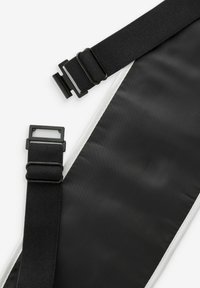 Sort nylonrem med to justerbare plastikspænder og hvid syning langs kanten. Glat tekstur, flad design.