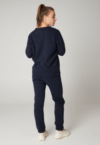 Felpa blu navy con collo rotondo e maniche a costine, abbinata a pantaloni jogger coordinati. Realizzata in tessuto morbido, adatta per l'abbigliamento casual.