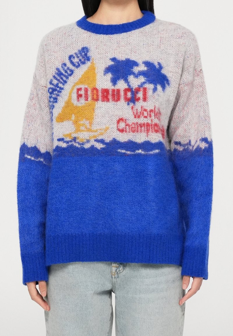 Pull avec bas bleu, haut gris, voilier jaune, palmiers bleus et texte rouge indiquant "Fiorucci World Champion Surfing Cup."