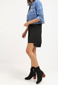 Džínová bunda v světle modré barvě, černé šaty a černé kotníkové boty s texturovaným povrchem a dřevěnými podpatky. Slim fit a ležérní design.
