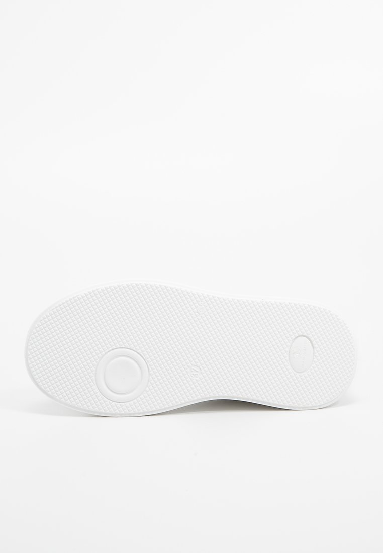Suela de zapatilla blanca con superficie de goma texturizada, que presenta acentos circulares y ovalados, y un diseño limpio y minimalista.