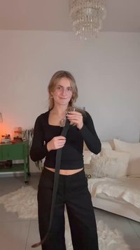 Sort stofbælte med en sølvfarvet cirkulær spænde, holdt af en person iført en sort langærmet top og sorte bukser, i et lyst rum.