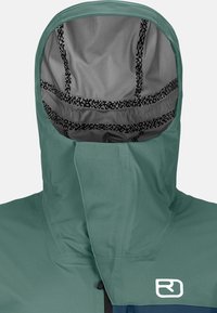 Hooded jacket in teal and navy, with a textured gray interior, featuring a logo on the chest and a snug-fitting hood design.
