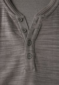 Camiseta henley texturizada gris con una tapeta que cuenta con tres botones oscuros y un cuello acanalado, fabricada con una tela suave y ligera.